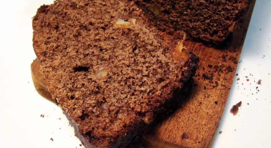 Rebanadas de pan de chocolate húmedo y denso, con trozos de fruta confitada, servidas en una tabla de madera.