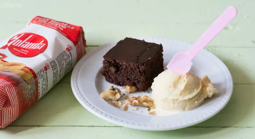 Un delicioso brownie sin huevo con helado de vainilla y nueces, junto a un paquete de Yolanda.