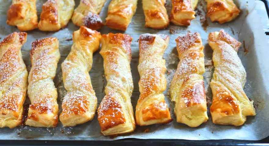 Deliciosos lazos de hojaldre dorados y espolvoreados con azúcar glas, listos para disfrutar.