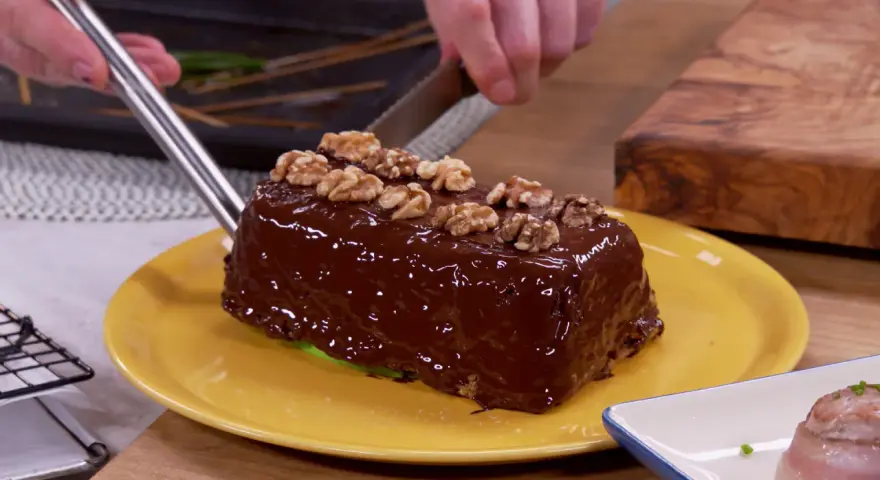 Un delicioso bizcocho de plátano cubierto de chocolate brillante y nueces, listo para ser cortado.