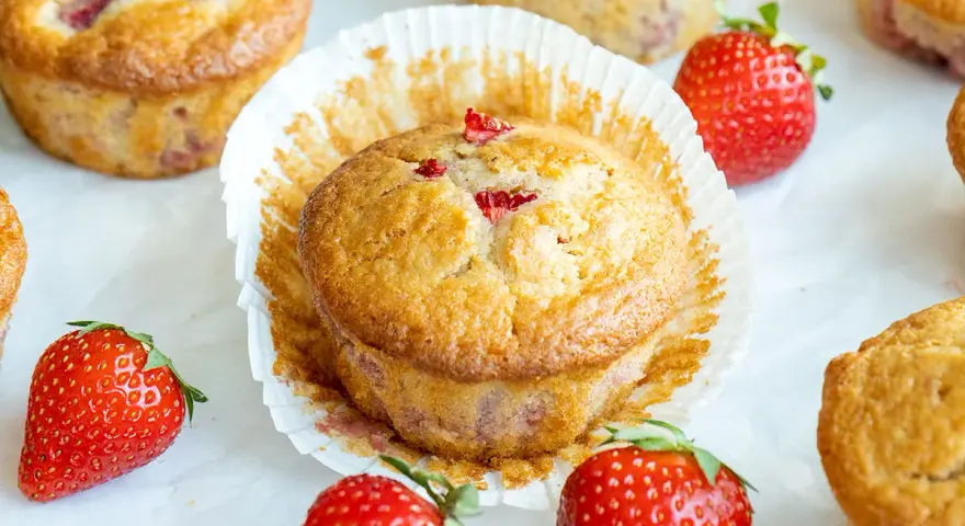 Delicioso postre con fresas, muffins dorados con trozos de fresa y fresas frescas alrededor.