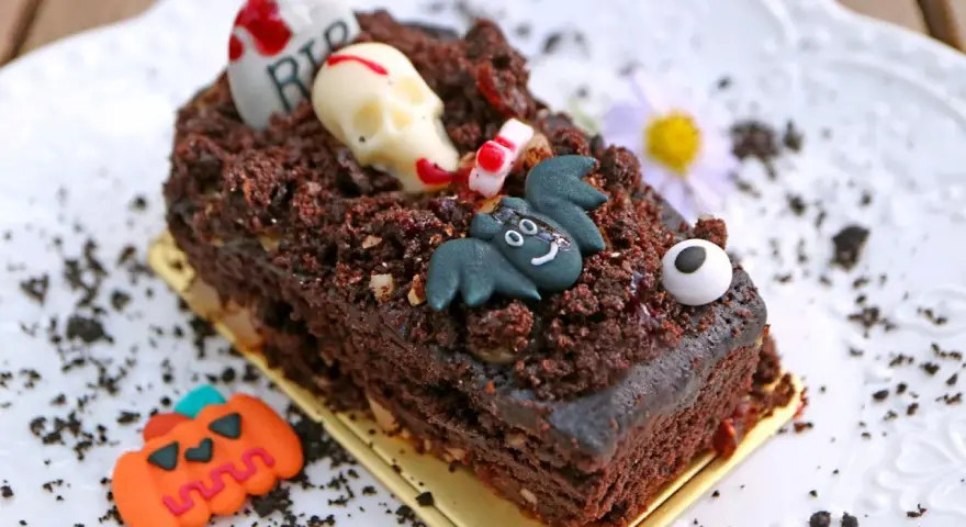 Tartas de Halloween originales: un pastel de chocolate cubierto de tierra de galleta, con un cráneo, un murciélago y una lápida.