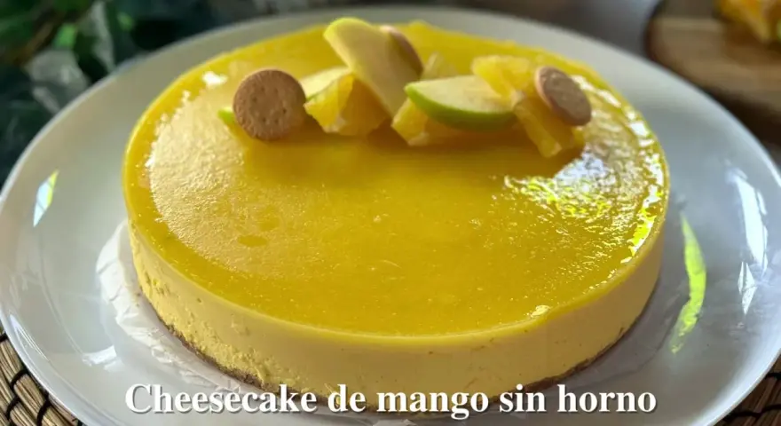 Tarta de queso y mango sin horno, decorada con trozos de manzana, naranja y galletas. ¡Un postre refrescante y delicioso!