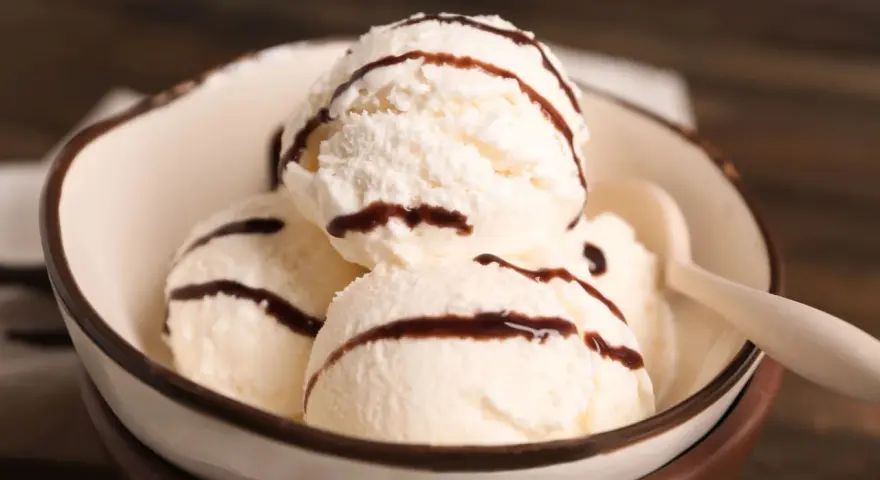 Cuatro bolas de helado de chocolate blanco con sirope de chocolate en un cuenco.