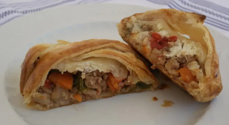 Hojaldre con carne picada y verduras, cortado por la mitad, mostrando el relleno jugoso.