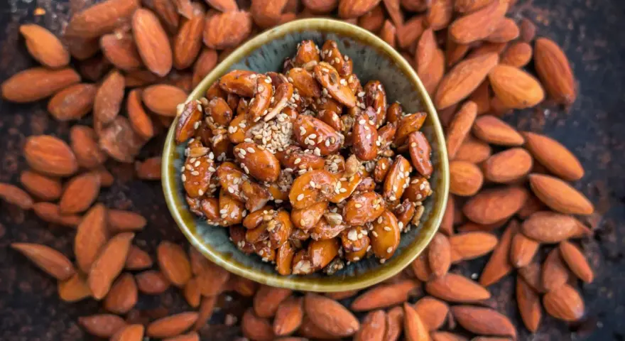 Un cuenco lleno de almendras caramelizadas, cubiertas de semillas de sésamo, rodeadas de almendras enteras.