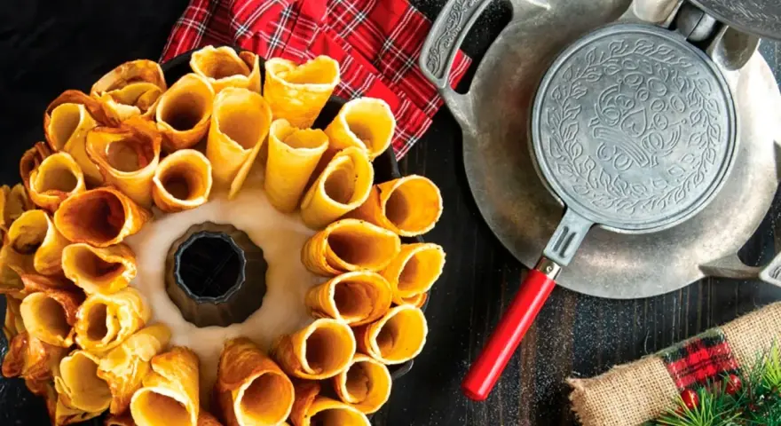 Deliciosos postres noruegos en forma de conos dorados, listos para rellenar. Una vieja gofrera de hierro reposa cerca.