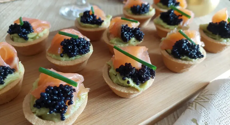 Deliciosas tartaletas de salmón y aguacate, coronadas con caviar negro y cebollino. Un bocado elegante y sabroso.