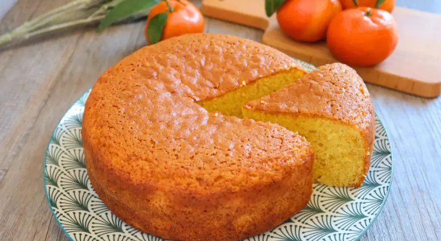 Bizcocho de mandarina y yogur, esponjoso y dorado, con una porción cortada. Mandarinas frescas al fondo.