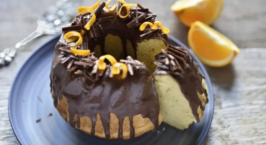 Bizcocho de chocolate y naranja, cubierto con glaseado de chocolate, virutas de chocolate y cáscara de naranja.