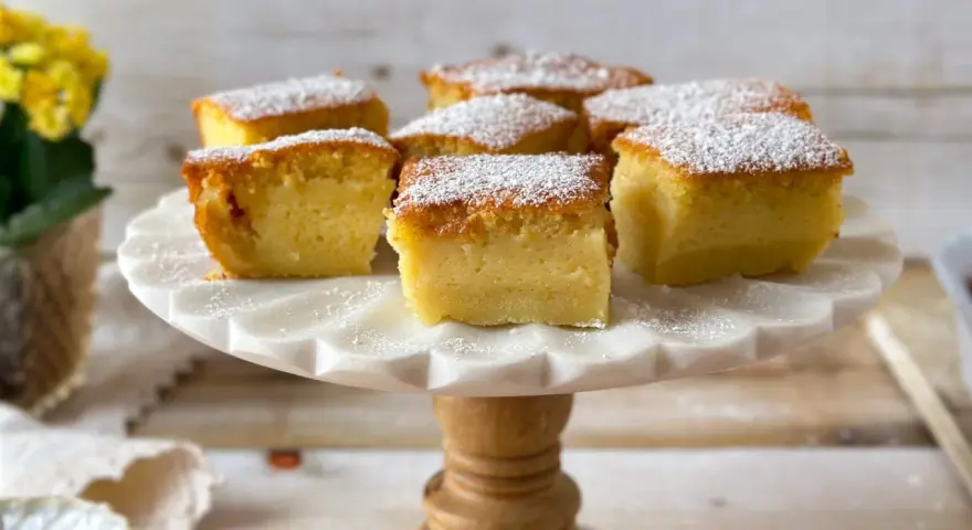 Porciones de un pastel mágico, cubiertas con azúcar glas, sobre un soporte de mármol.