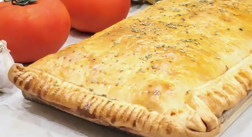 Empanada de pisto dorada y crujiente, con tomates frescos y ajo al lado. ¡Un manjar casero!