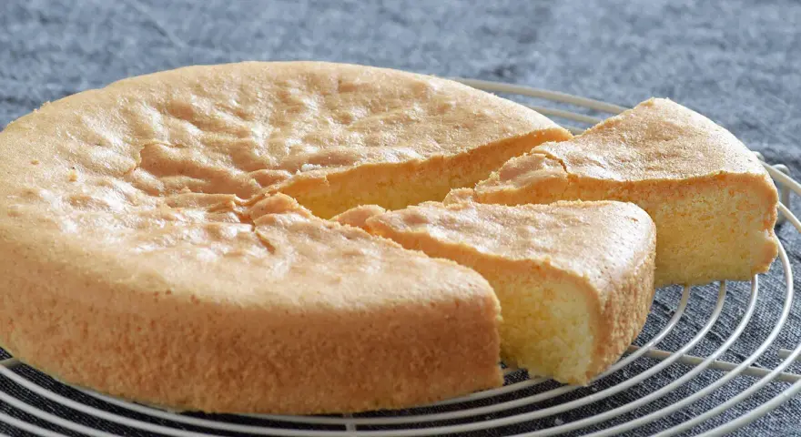 Un esponjoso bizcocho sin gluten, recién horneado y cortado en porciones, descansa sobre una rejilla.