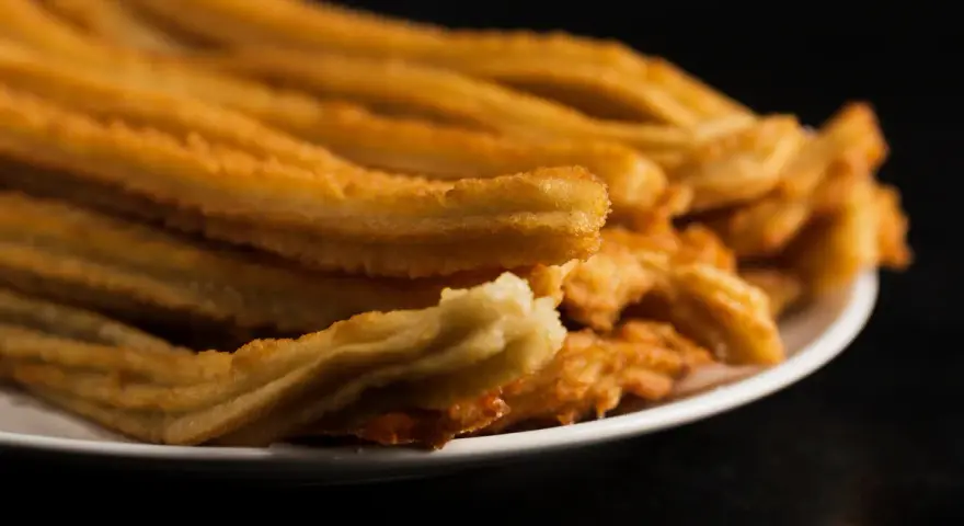 Montón de churros de patata dorados y crujientes apilados en un plato blanco.