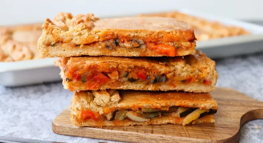 Tres porciones de empanada de verduras apiladas, mostrando el relleno de pimientos, calabacín y tomate.