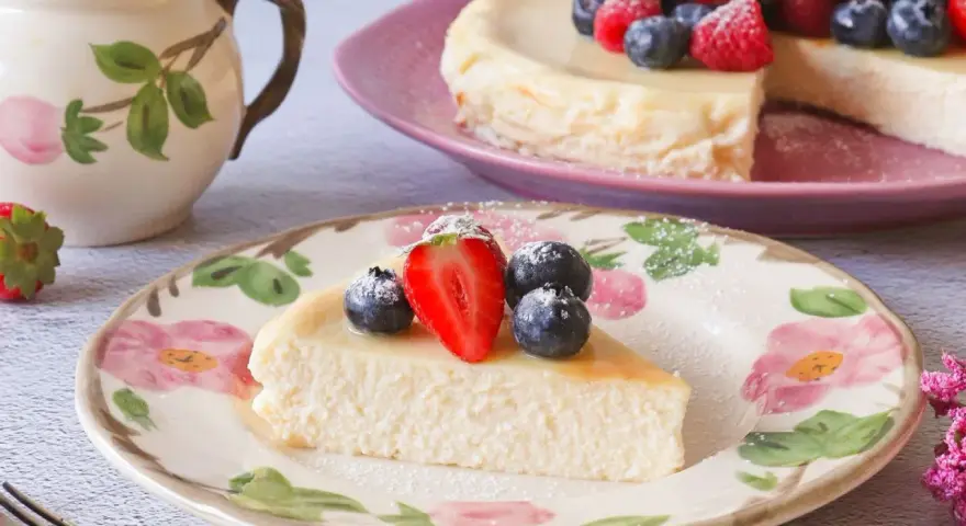 Deliciosa tarta de requesón, decorada con fresas y arándanos, servida en un plato floral.