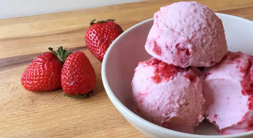 Delicioso helado de frutos rojos con fresas frescas al lado, listo para disfrutar en un día caluroso.