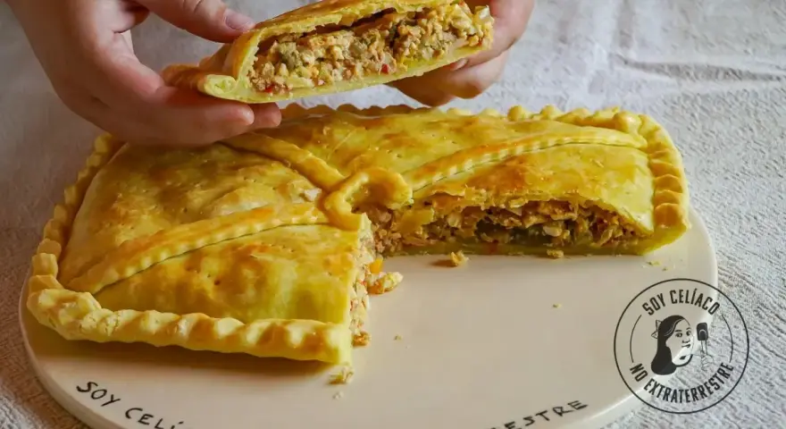 Una mano levanta un trozo de empanada de carne dorada y rellena. La masa crujiente envuelve un sabroso guiso.