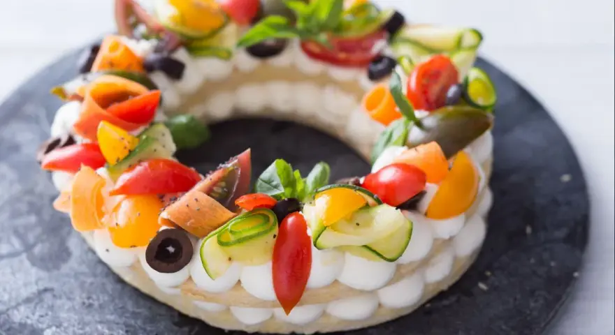 Deliciosa cream tart circular adornada con tomates, pepino, aceitunas y albahaca.