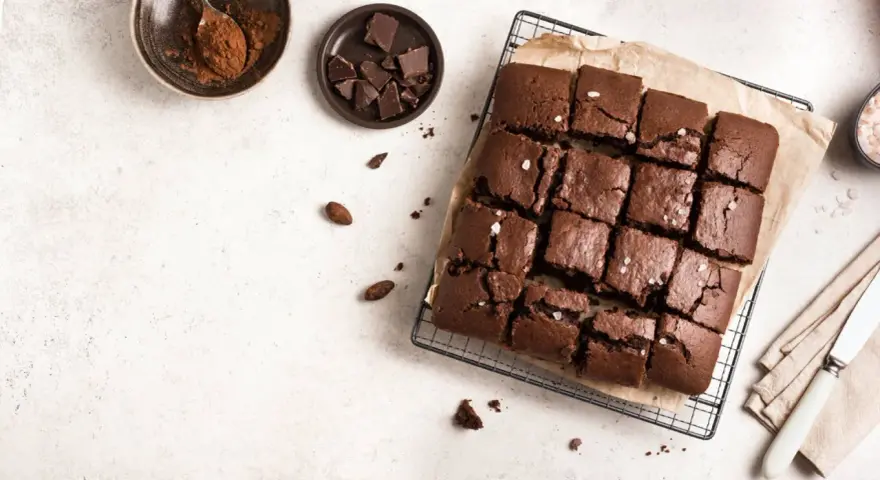Delicioso brownie sin horno, cortado en cuadrados y espolvoreado con sal marina. Ingredientes como cacao y chocolate en trozos acompañan esta tentación.