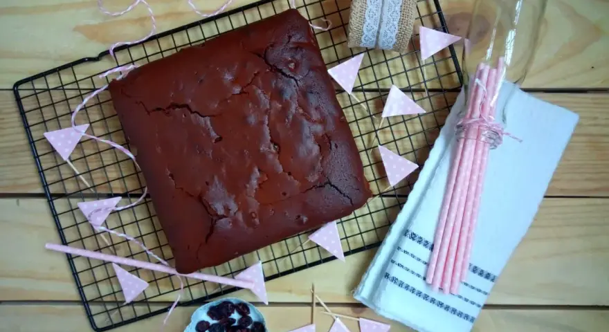 Un delicioso brownie recién horneado, listo para ser cortado. Decorado con banderines rosas y arándanos.