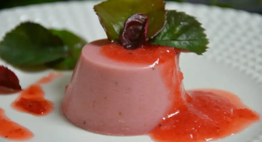 Delicioso panna cotta de fresa, bañado en salsa de fresa y decorado con hojas verdes.