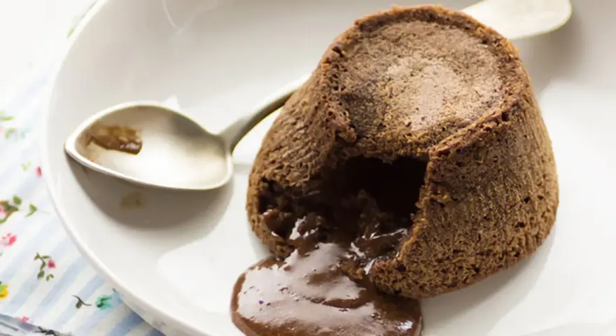 Coulant de chocolate recién horneado, con su interior líquido de chocolate derretido, listo para ser disfrutado con una cuchara.
