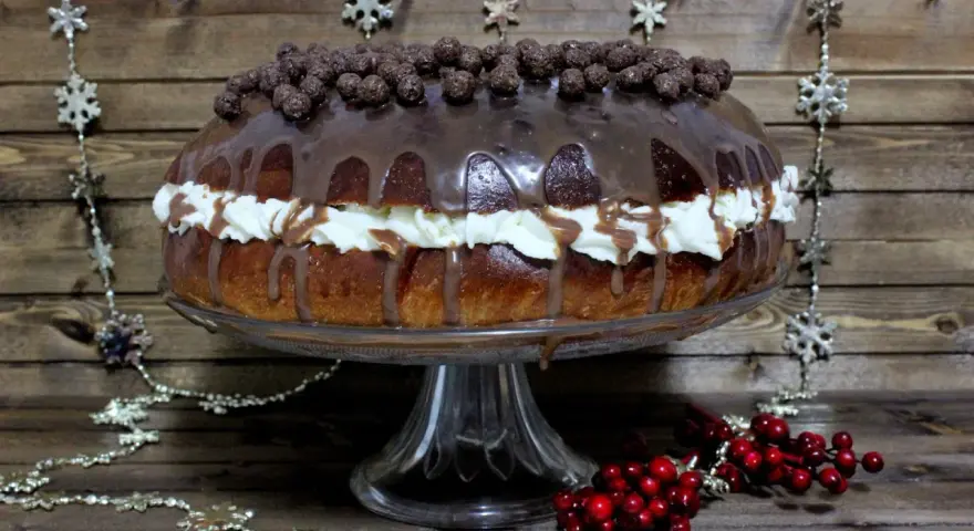 Un delicioso roscon de reyes chocolate, cubierto de glaseado y bolitas de chocolate, con crema y decoraciones navideñas.