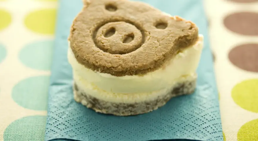 Un delicioso helado de galleta con forma de cerdito, servido sobre una servilleta azul turquesa.