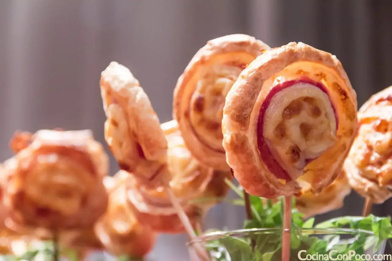 Deliciosas piruletas de hojaldre rellenas de queso y jam&oacute;n, perfectas para un aperitivo.