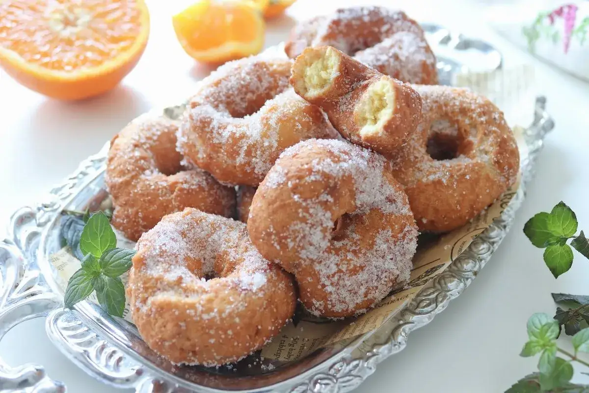 Rosquillas de naranja reci&eacute;n hechas, cubiertas de az&uacute;car, servidas en una bandeja plateada.