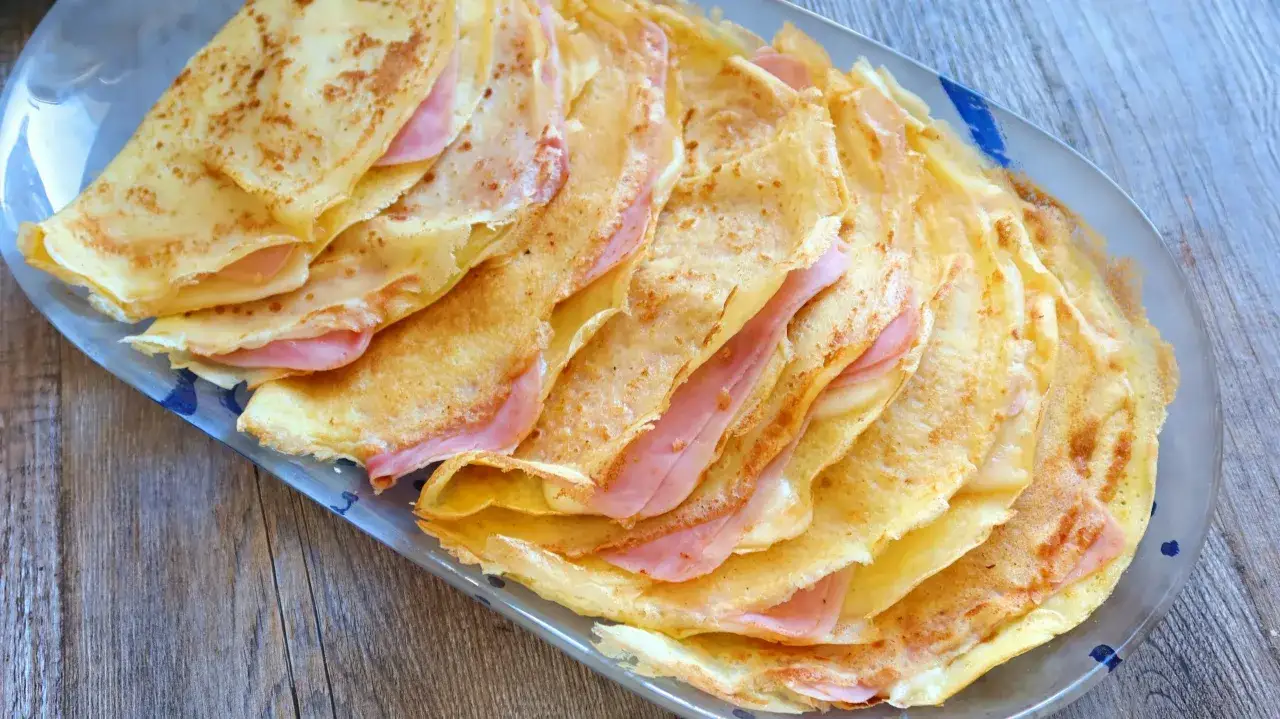 Crepes sin gluten rellenos de jam&oacute;n y queso, apilados en una bandeja.