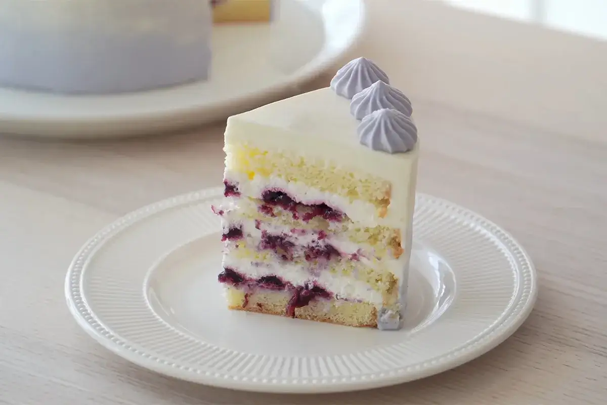Deliciosa tarta de chocolate blanco con capas de bizcocho esponjoso, crema y ar&aacute;ndanos. Decorada con merengues morados.