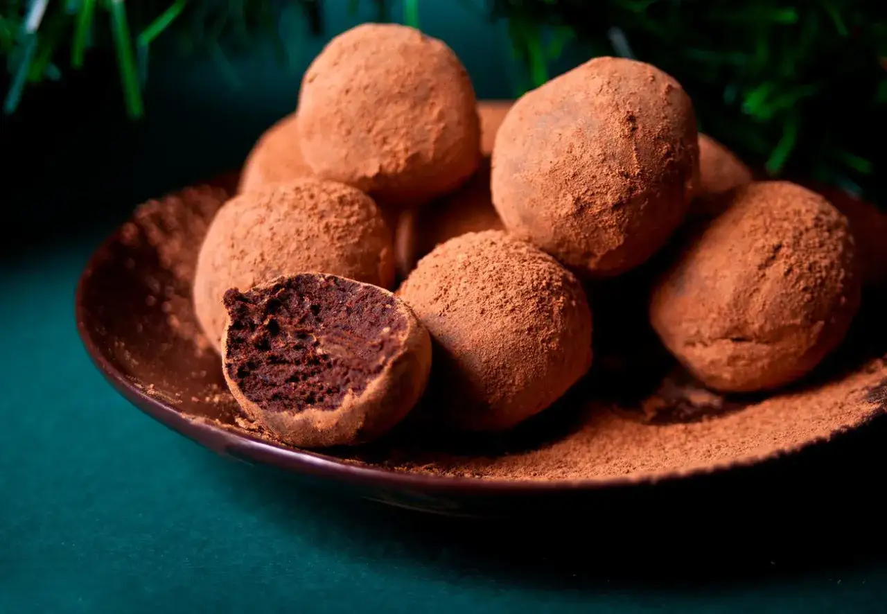 Mont&oacute;n de trufas de chocolate cubiertas de cacao en polvo, una partida por la mitad revela su interior oscuro y rico.