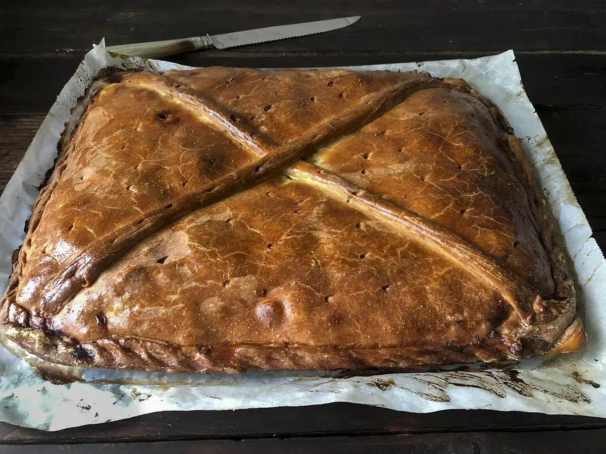 Empanada de at&uacute;n dorada y crujiente, lista para ser cortada. Su masa presenta un dise&ntilde;o cruzado y bordes trenzados.
