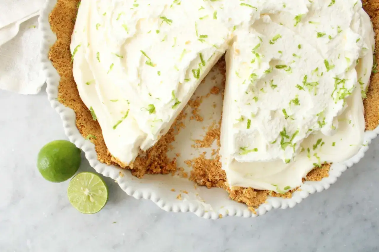 Delicioso key lime pie con crema batida y ralladura de lima, listo para disfrutar.