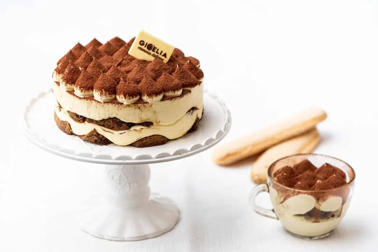 Un delicioso helado de tiramis&uacute; en un plato blanco, acompa&ntilde;ado de bizcochos de soletilla y una copa con la misma delicia.