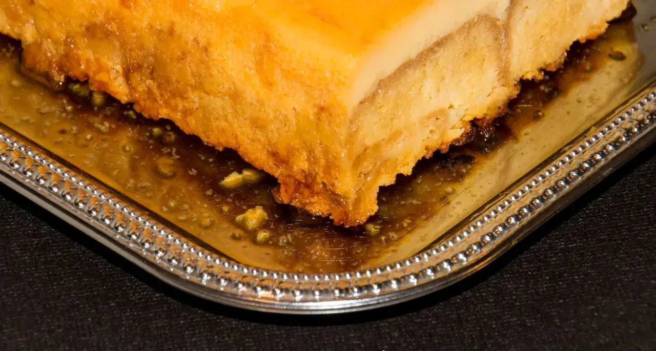 Un trozo de pastel de maiz dorado y h&uacute;medo, ba&ntilde;ado en un sirope dulce, servido en una bandeja plateada con borde decorado.