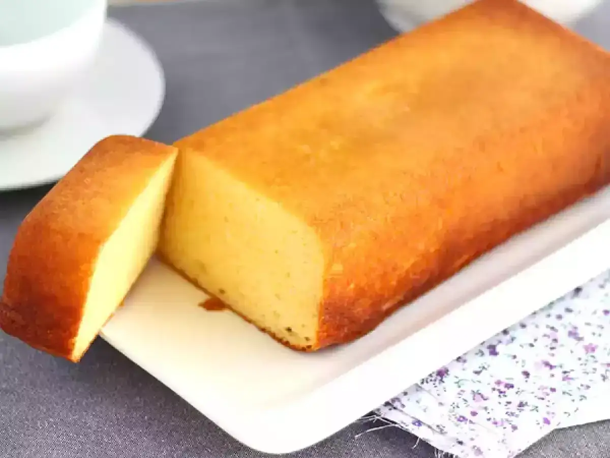 Un delicioso bizcocho de leche condensada, dorado y esponjoso, servido en una bandeja blanca con una porci&oacute;n cortada.