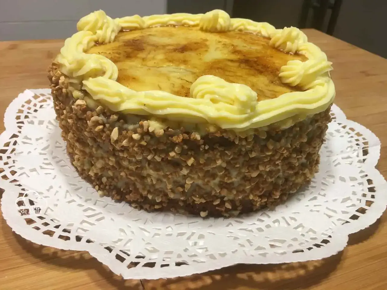 Tarta de crema con bordes cubiertos de frutos secos y un glaseado dorado en la parte superior, decorada con rosetones de crema.