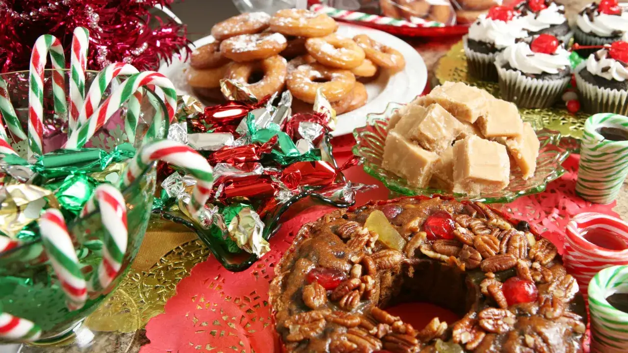 Una mesa llena de deliciosos postres navideños: pastel de frutas, fudge, donas, cupcakes y bastones de caramelo.