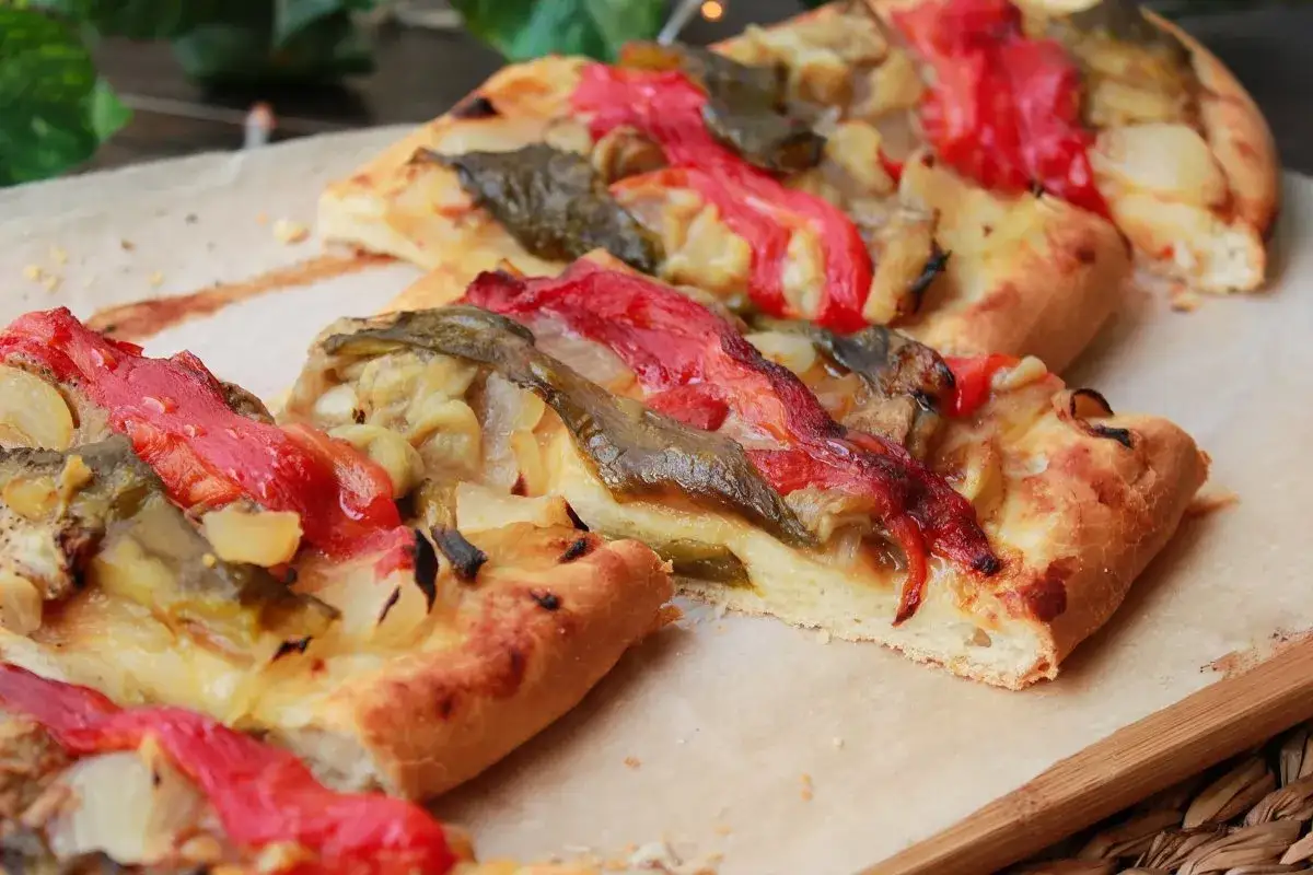 Deliciosa coca de recapte con pimientos rojos y verdes asados, cebolla y queso fundido sobre una base crujiente.