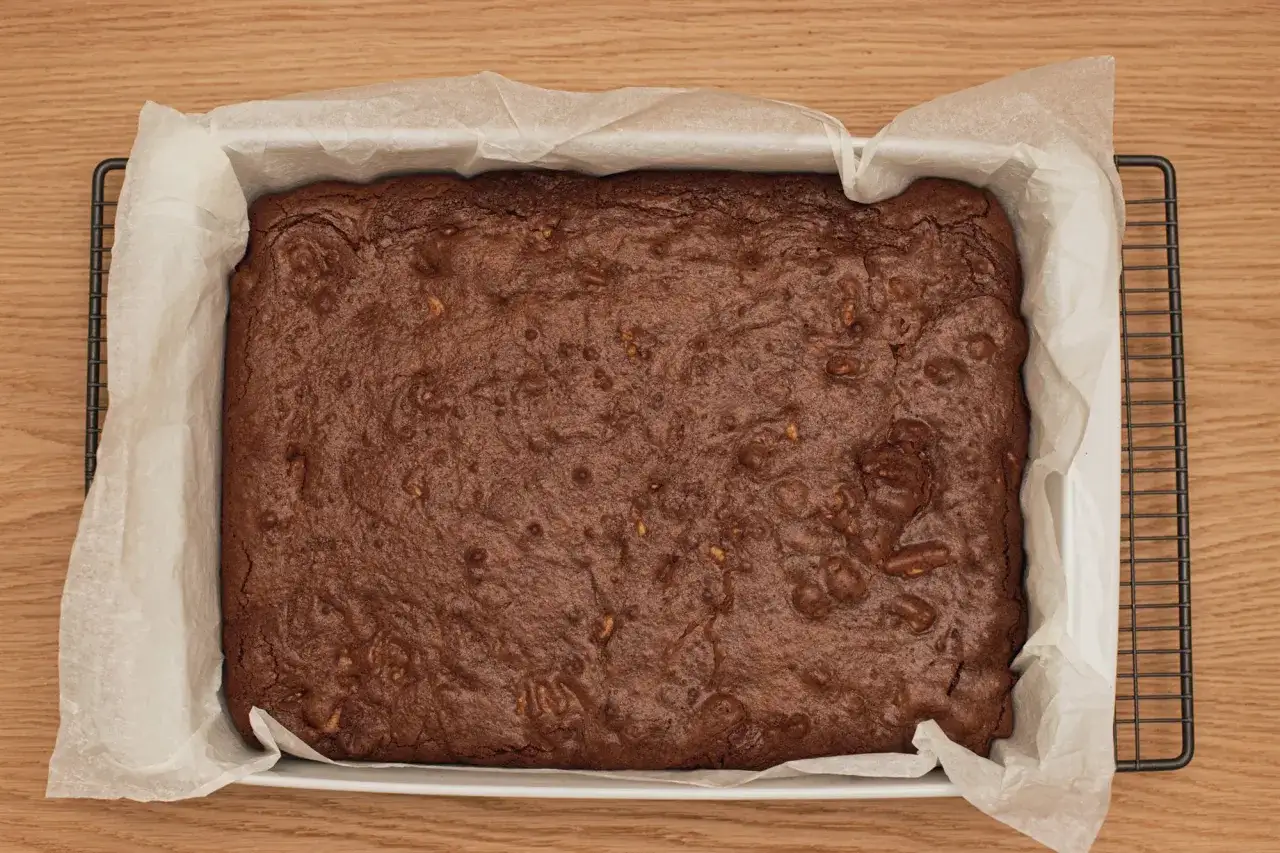 Brownie reci&eacute;n horneado, listo para enfriar. La superficie crujiente y los trozos de nuez prometen una deliciosa receta de brownie esponjoso.