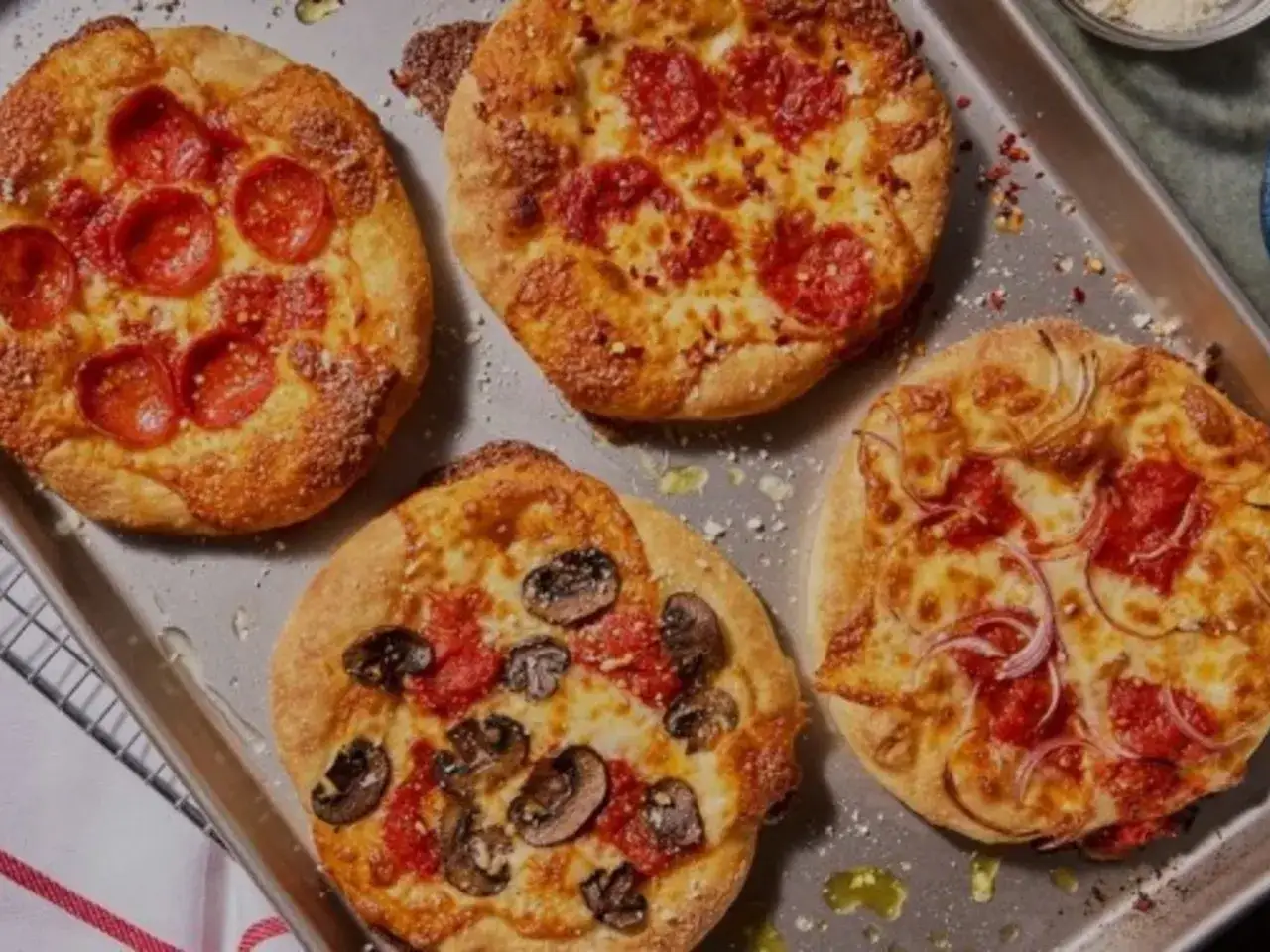 Cuatro mini pizzas reci&eacute;n horneadas en una bandeja: una con pepperoni, otra con champi&ntilde;ones y dos con pepperoni y cebolla. &iexcl;Perfectas para compartir!