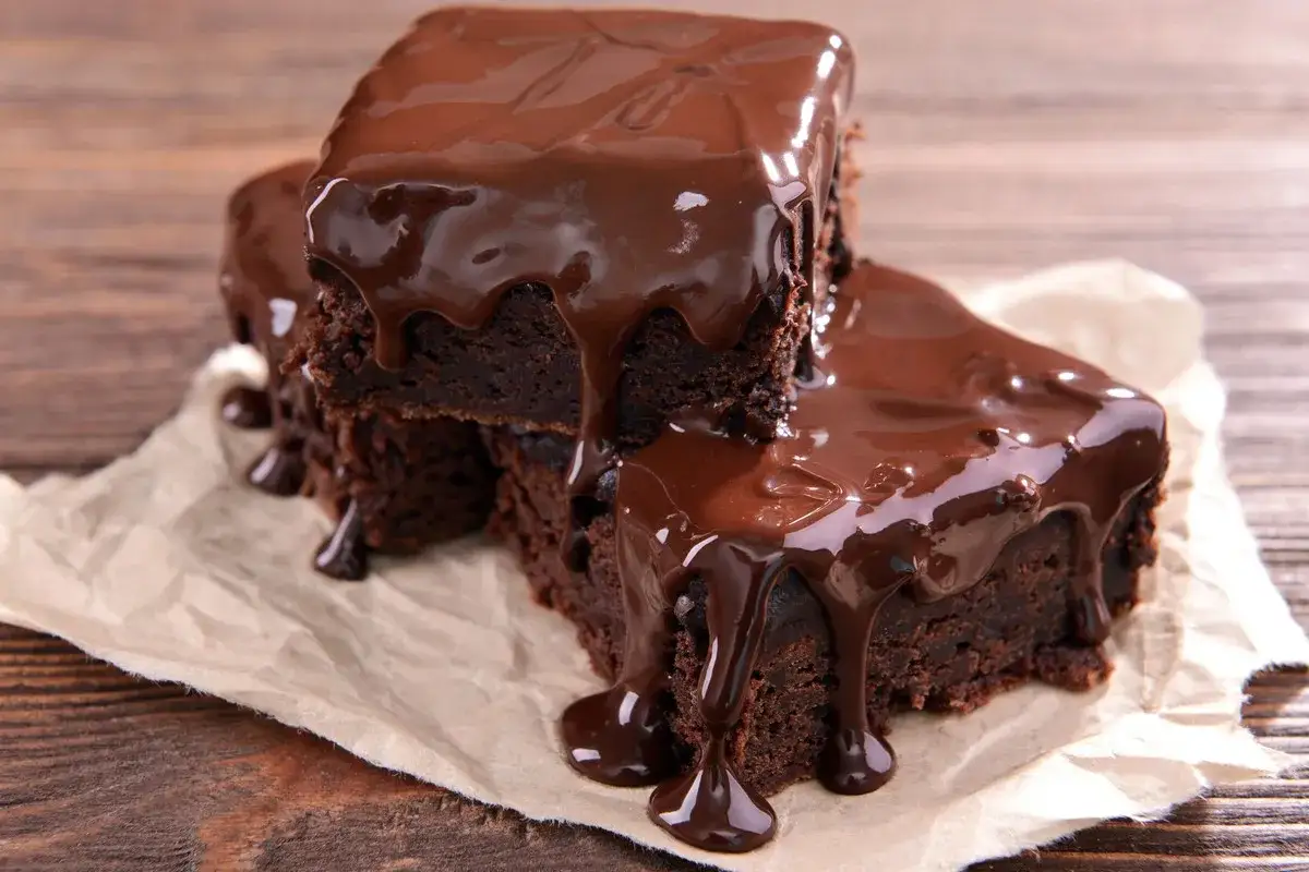 Deliciosos postres de chocolate, brownies cubiertos con glaseado de chocolate derretido, goteando sobre papel de hornear.