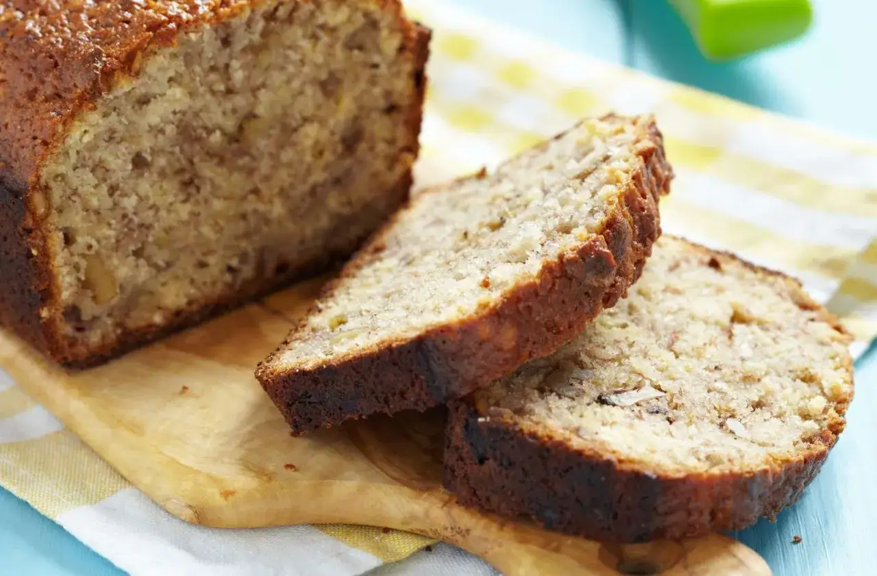 Rebanadas de un delicioso banana bread casero, con nueces visibles, sobre una tabla de madera y un paño a cuadros.