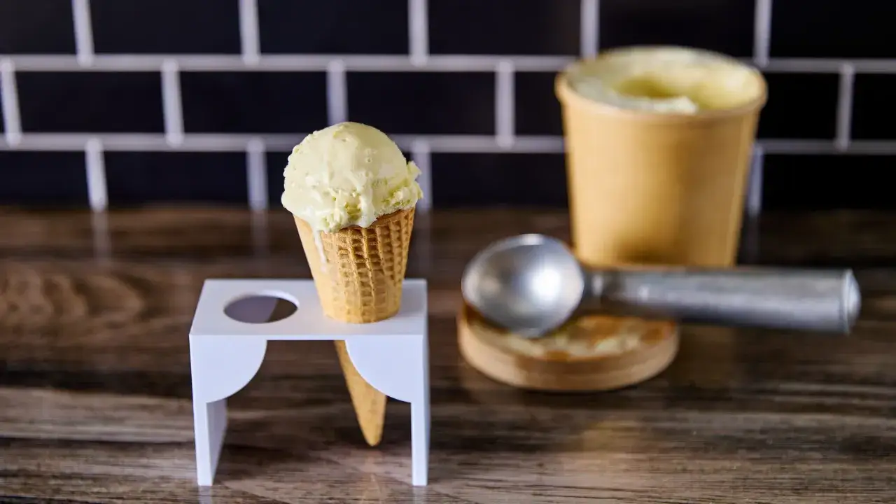 Un cono de helado de chocolate blanco cremoso, listo para disfrutar. A su lado, un cucharón y un recipiente con más helado.