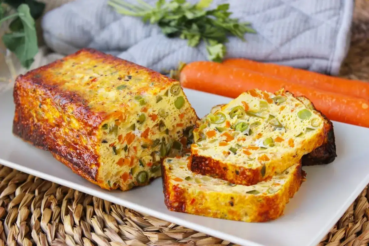 Un delicioso pastel de verduras, con trozos de zanahoria y guisantes, servido en una bandeja blanca.