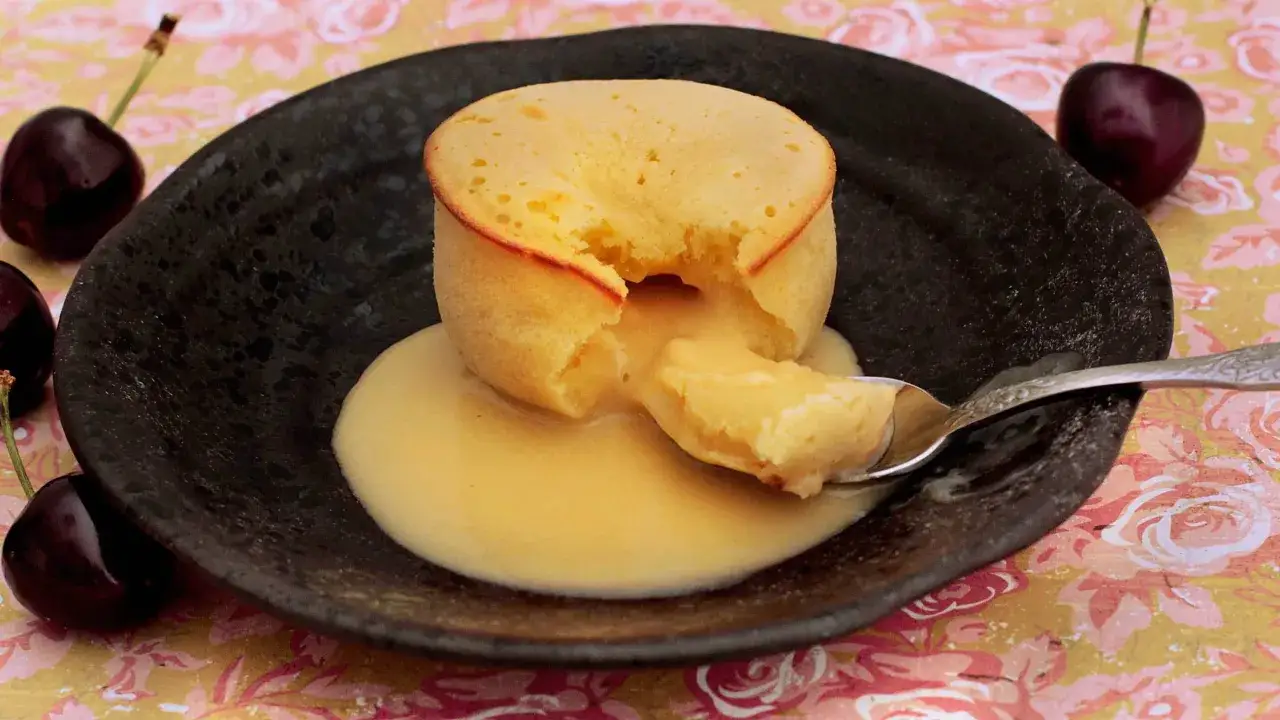Coulant de chocolate blanco con interior cremoso, servido en plato negro con cerezas.