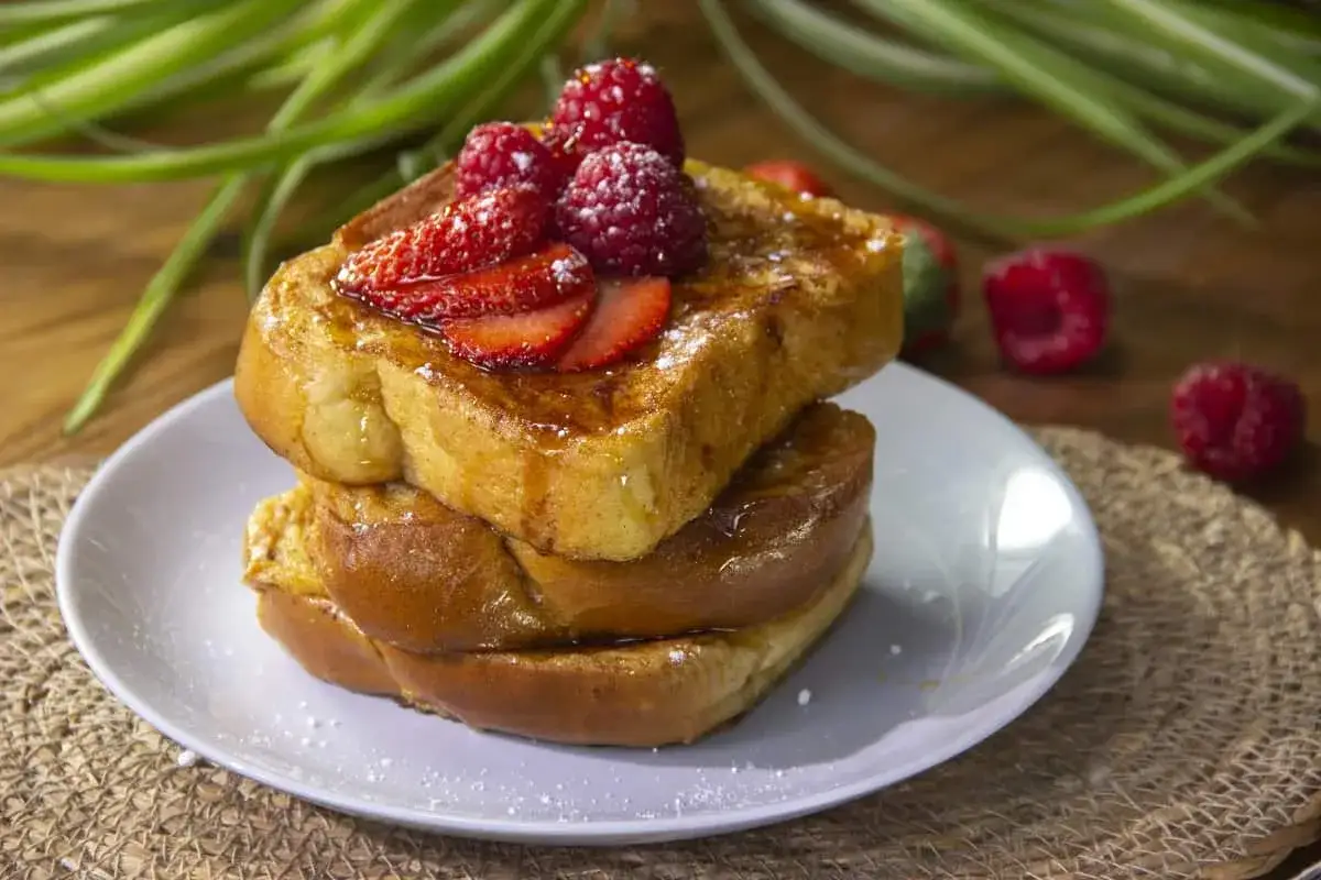 Tostadas francesas doradas y esponjosas, apiladas y cubiertas con fresas, frambuesas y un toque de azúcar glas.